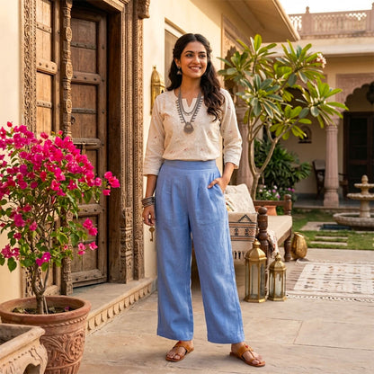 Woman standing in a decorative outdoor setting with flowers and traditional architecture.